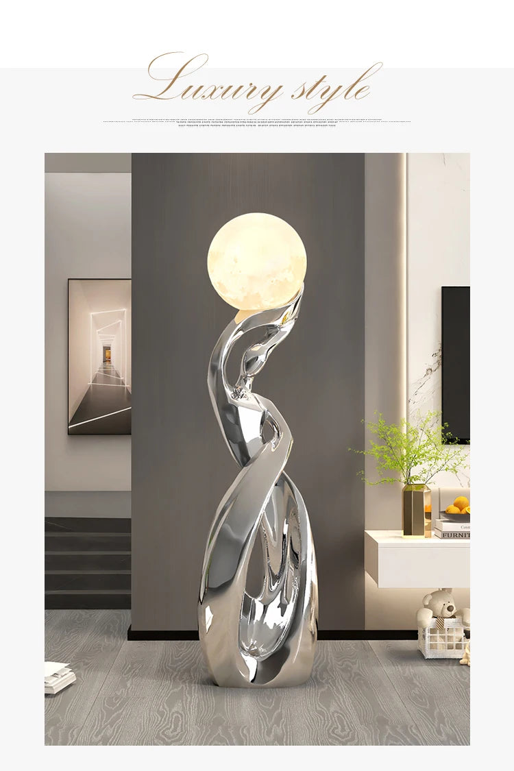 Tall abstract silver resin floor statue with a luminous, glowing moon-shaped sphere on top. Modern luxury design.