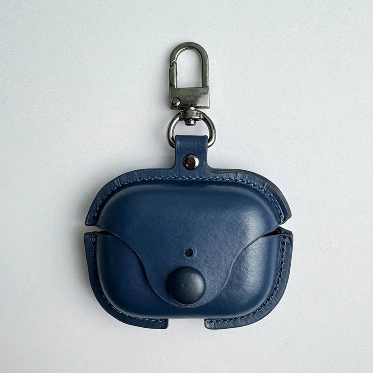 Navy blue leather AirPods Pro case with snap button closure and metal keychain clip on a white background.