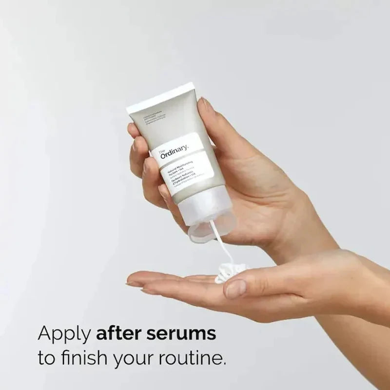 Hand squeezing a white moisturising cream from a grey, minimalist travel-sized tube into the palm of the other hand.