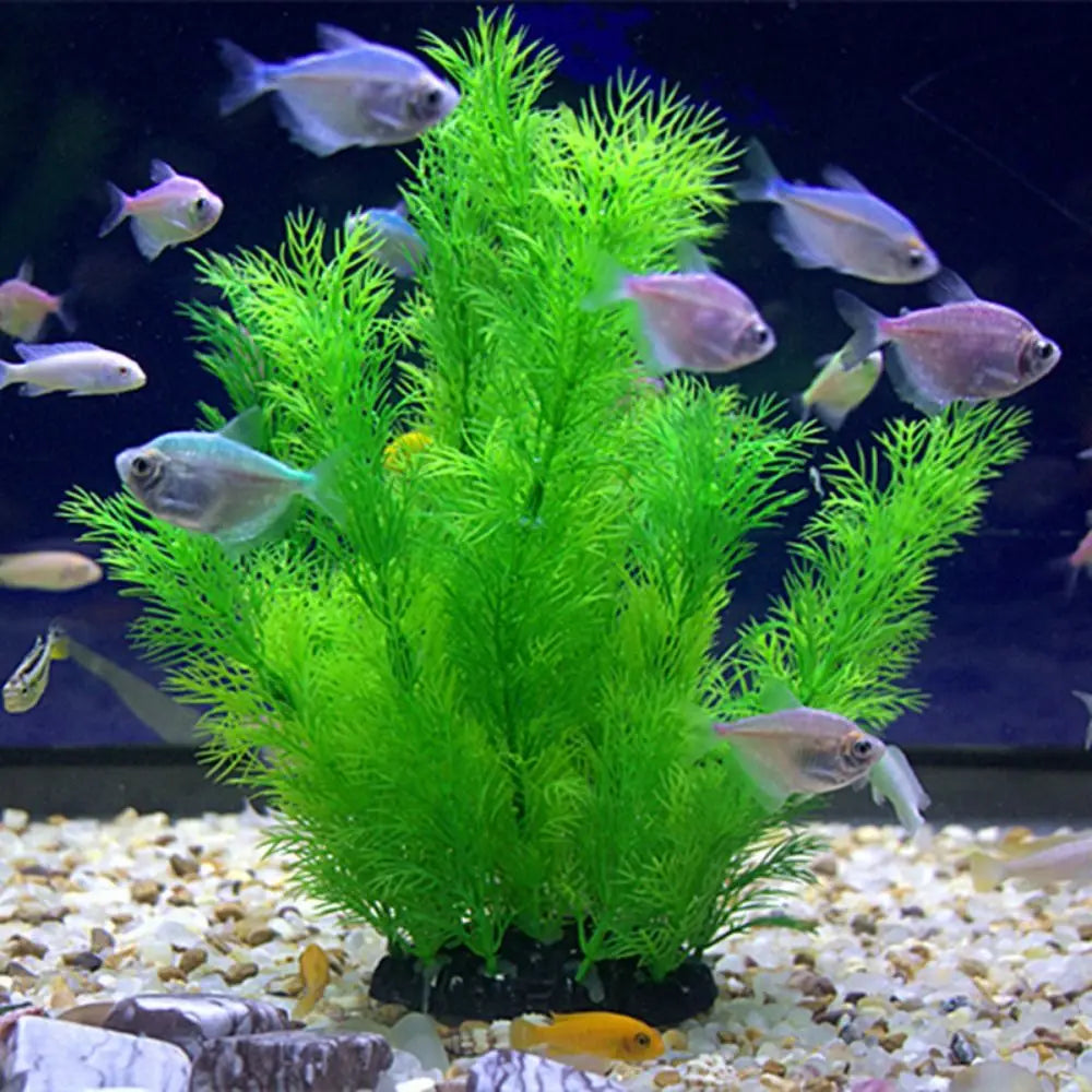 Bright green, feathery artificial aquarium plant surrounded by many small, silvery fish on a gravel tank floor.