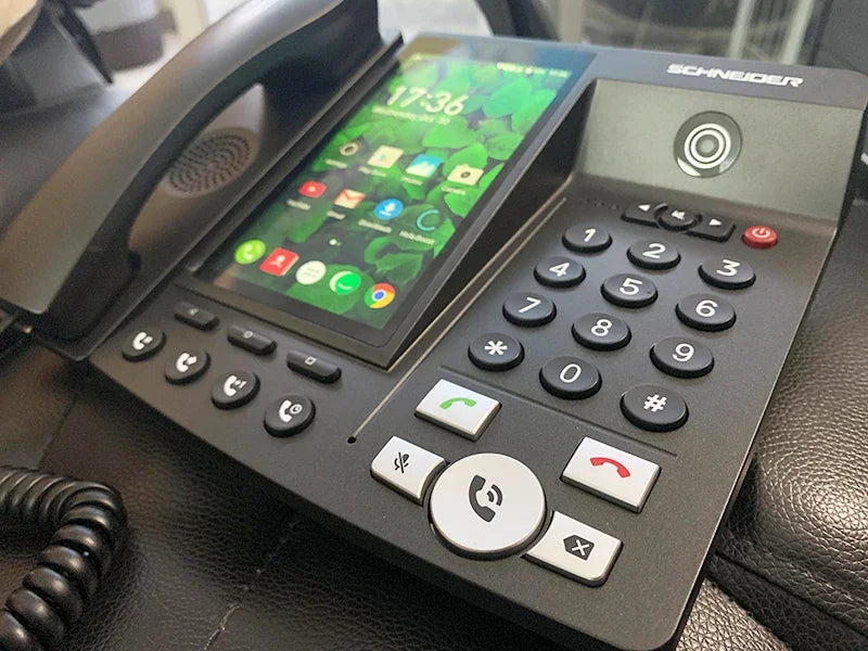 Black desk phone with a vertical touchscreen interface, physical keypad, and wired handset.
