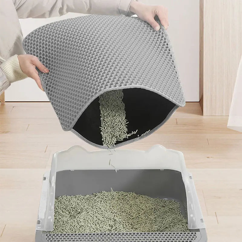 Grey, honeycomb-patterned double-layer cat litter mat being emptied into a tray to reuse trapped litter.