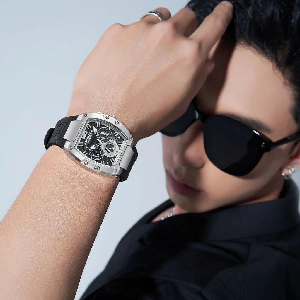 Silver tonneau wristwatch with a black dial and strap worn on a man's arm.