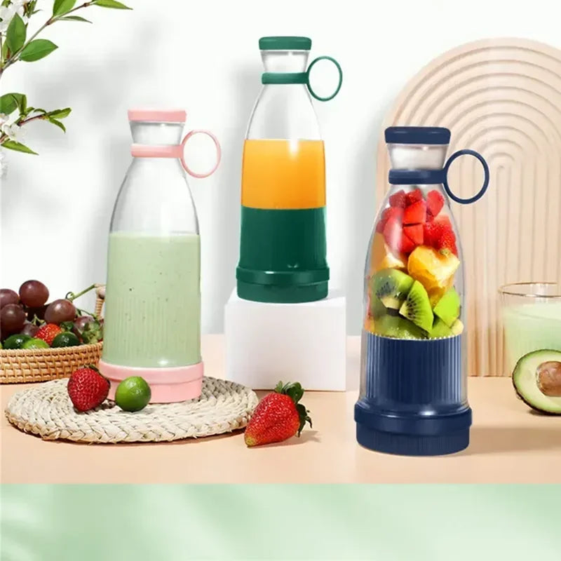 Three portable, cylindrical smoothie blenders in pink, green, and dark blue with carrying loops on a table.