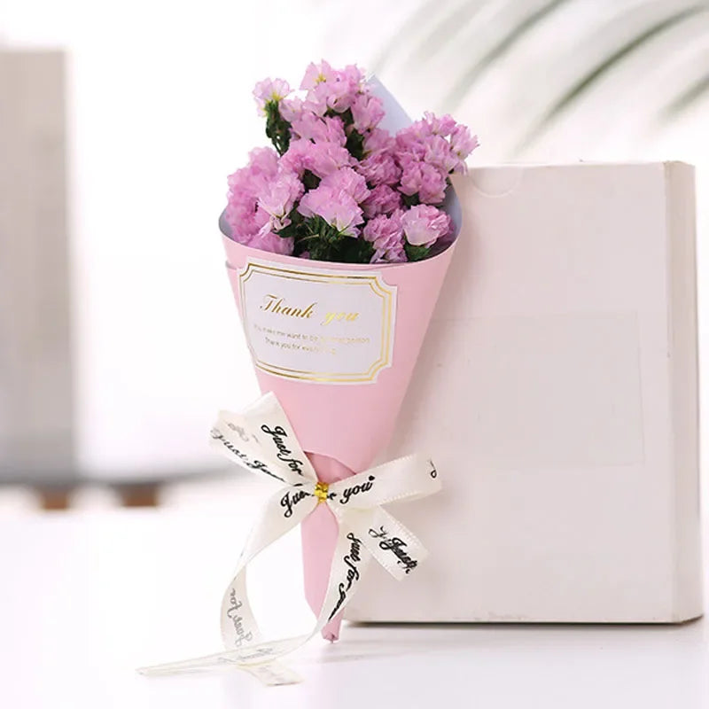 A small, charming bouquet of pale pink artificial flowers, wrapped in pink paper with a 'Thank you' ribbon.