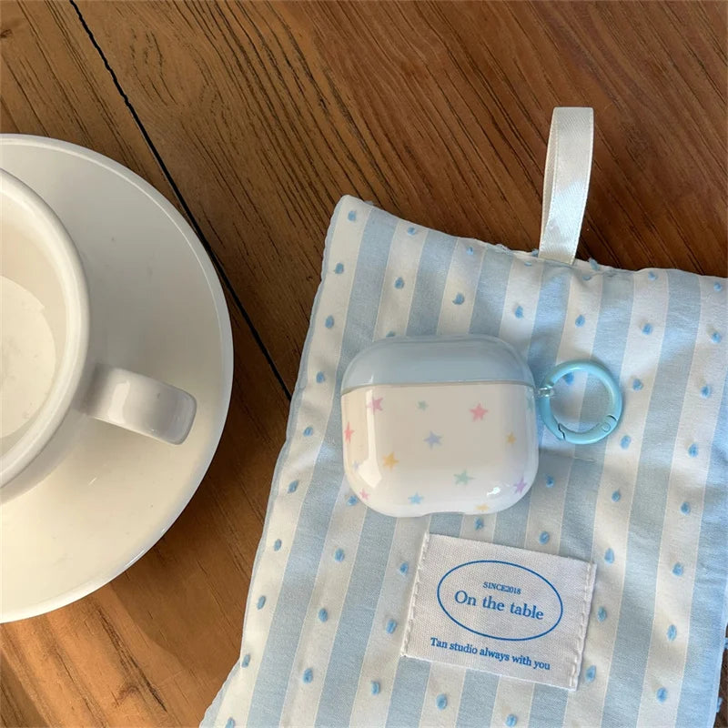 Clear AirPods case featuring a colourful star print, light blue trim, and matching carabiner.