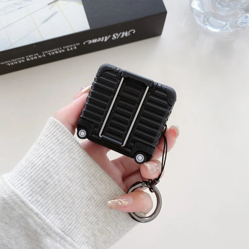 Black silicone AirPods case designed as a miniature suitcase with wheels and a metal keyring attachment.