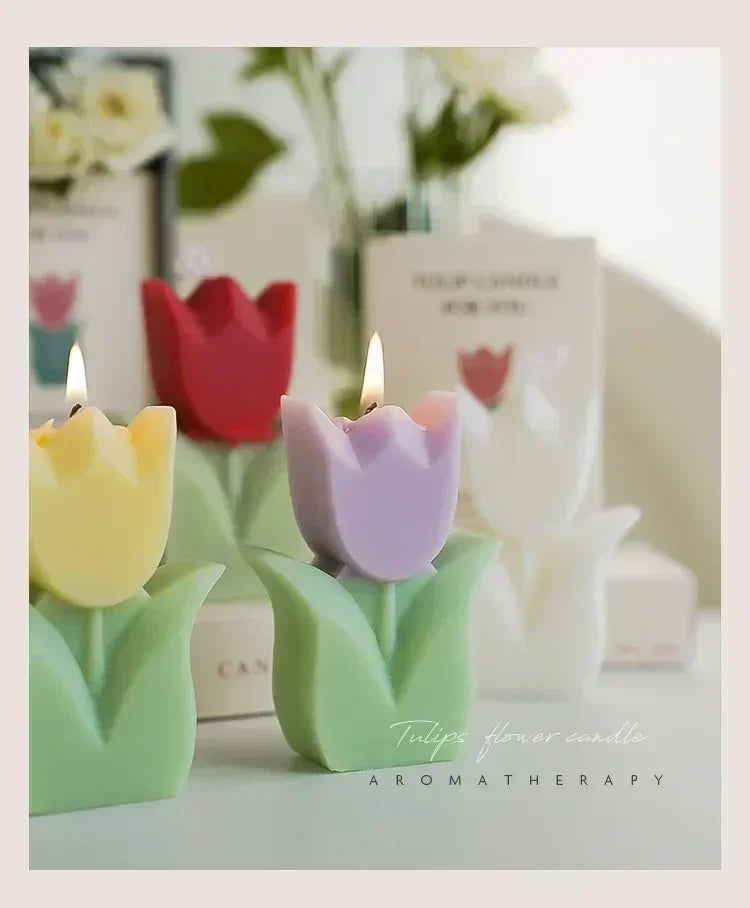 Decorative tulip-shaped candles in pastel yellow, red, and purple with green leaf bases, lit and set on a white table.