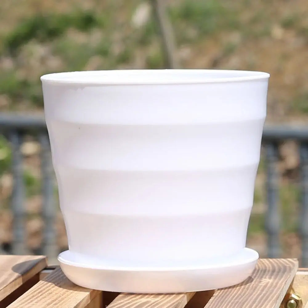 Empty white plastic flower pot with horizontal ridges, sitting on a matching saucer on a wooden surface.