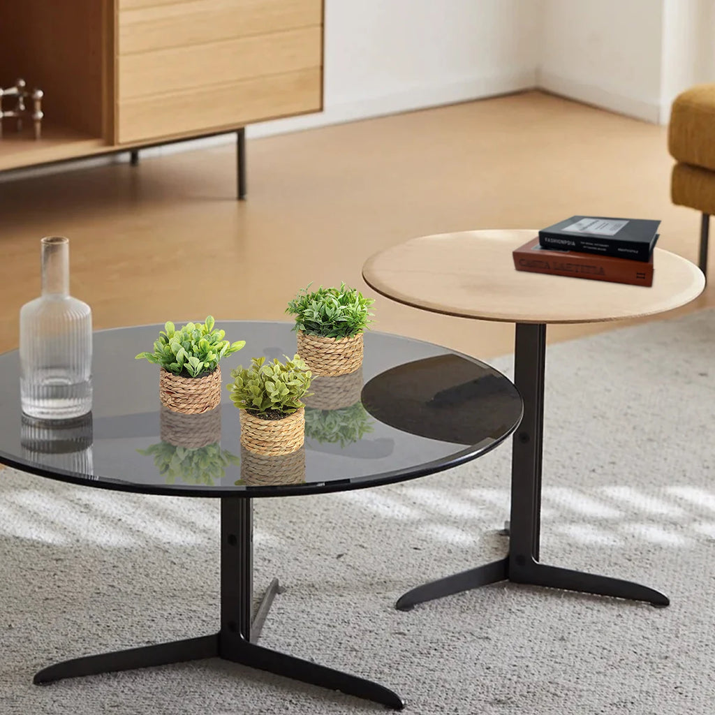 Three small artificial green eucalyptus plants in rustic woven grass pots sitting on a modern glass coffee table.