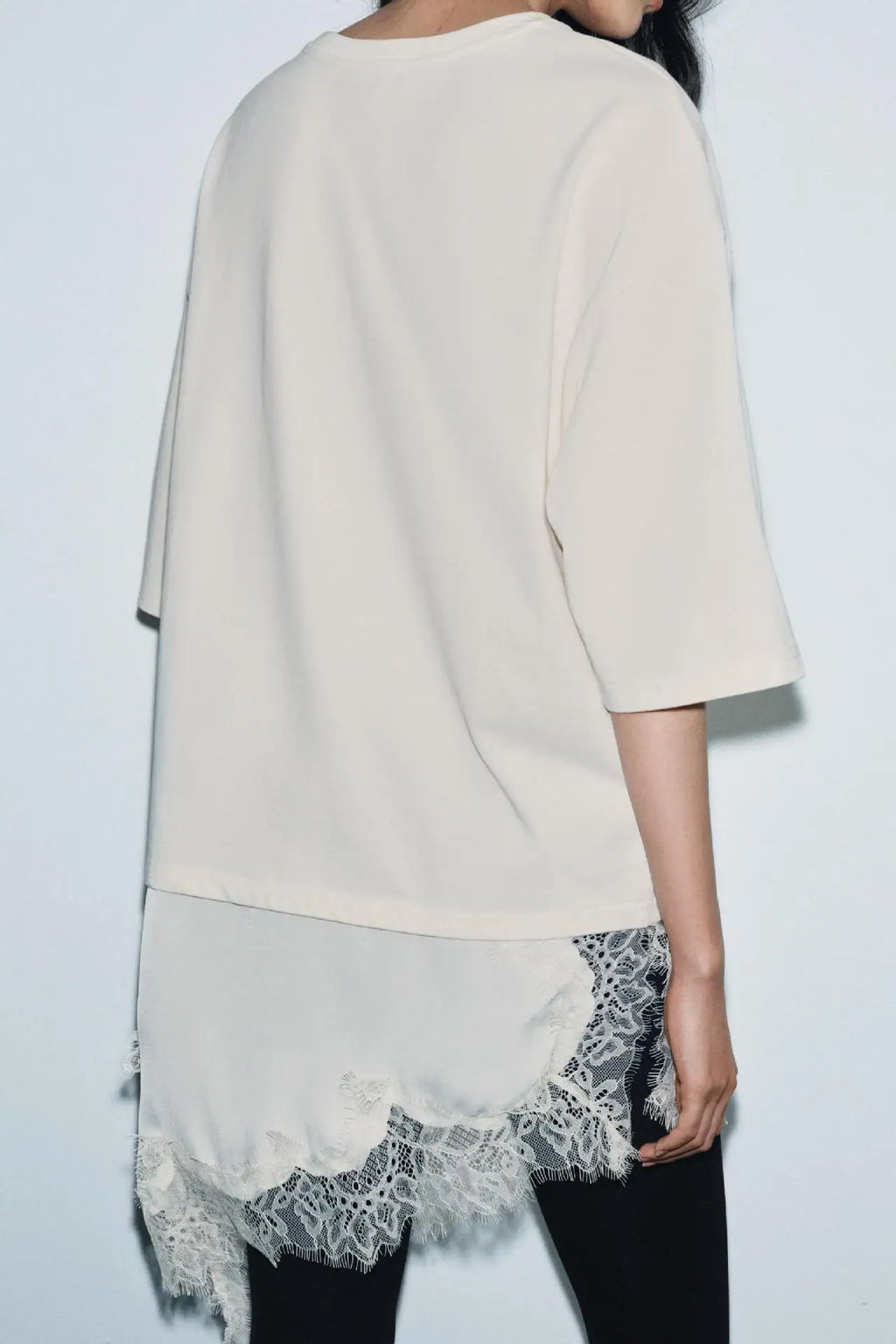 Cream-coloured short-sleeve top featuring a long, flowing asymmetrical hem with delicate lace trim detailing.