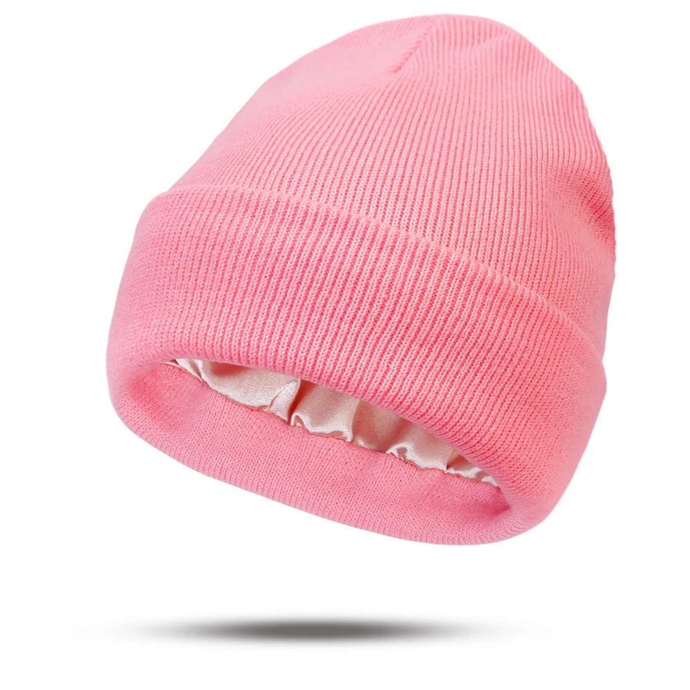 Bright pink knitted beanie hat with a smooth, champagne-coloured satin lining, isolated on a white background.
