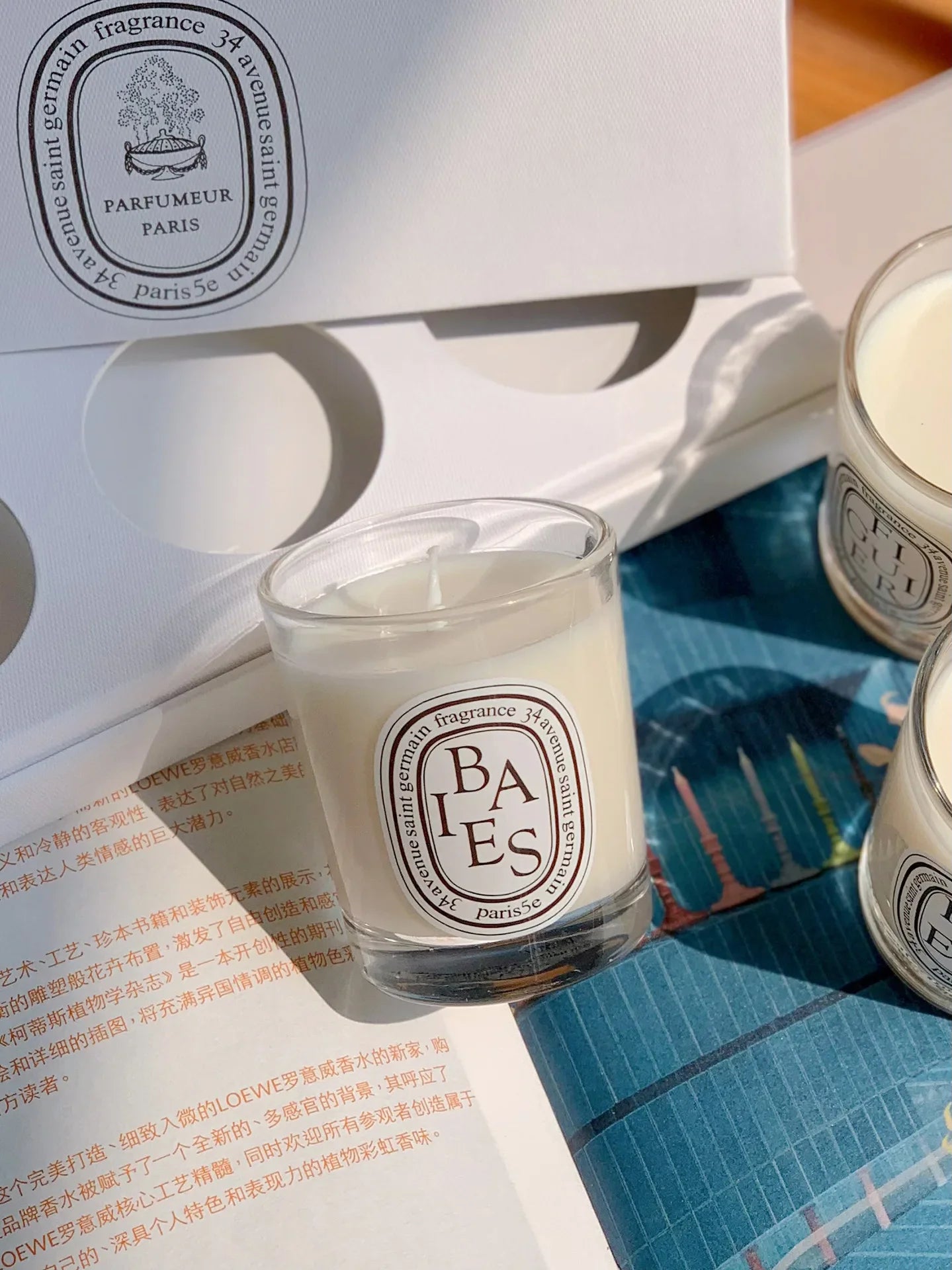 Small white scented candle in a clear glass jar with a decorative oval label, presented in a gift box.