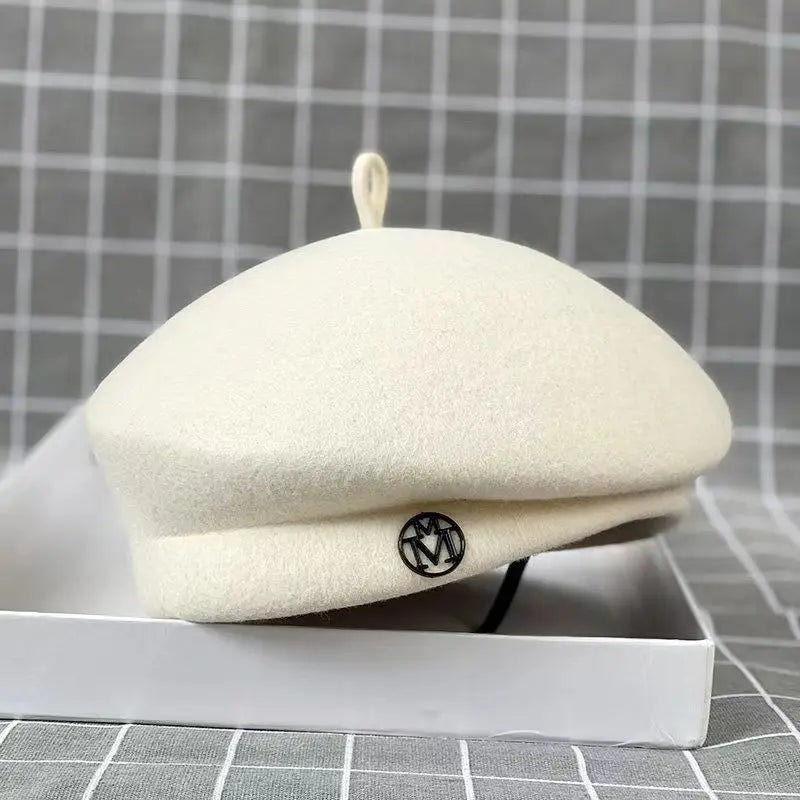 Cream-coloured wool felt beret with a small top loop and a circular metallic detail on the side.