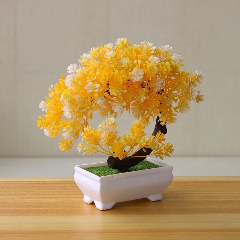 Artificial bonsai tree with yellow and white leaves in a small white rectangular pot on a wooden surface.