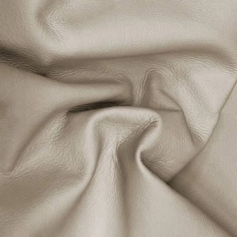 Close-up of premium, soft beige genuine leather with natural grain texture, used for upholstered furniture.
