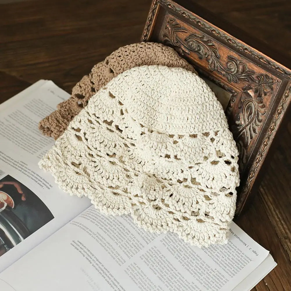 Two women's hollow crochet lace hats in cream and light brown, resting on an open book.