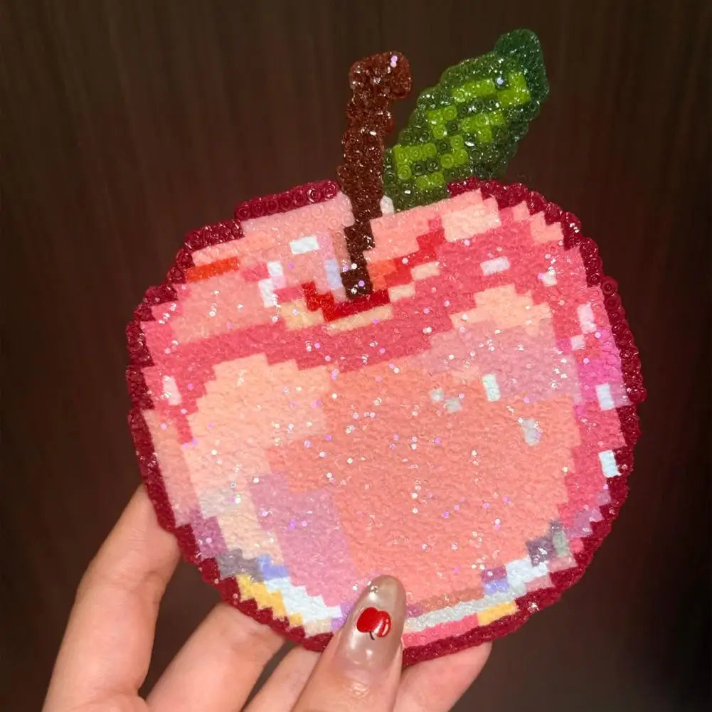 A hand holding a sparkling, pixel-art style apple patch in shades of pink with a brown stem and green leaf.