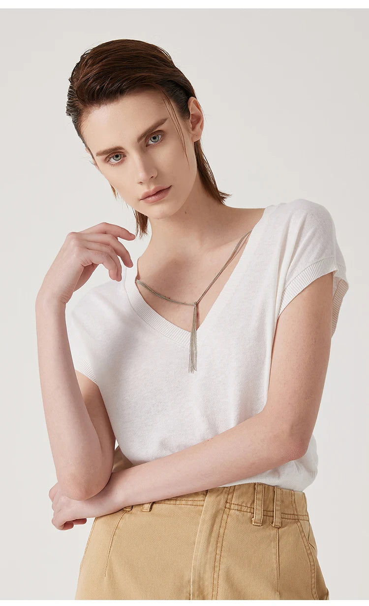 Model wears a white V-neck knitted t-shirt with short sleeves and a delicate silver chain detail.