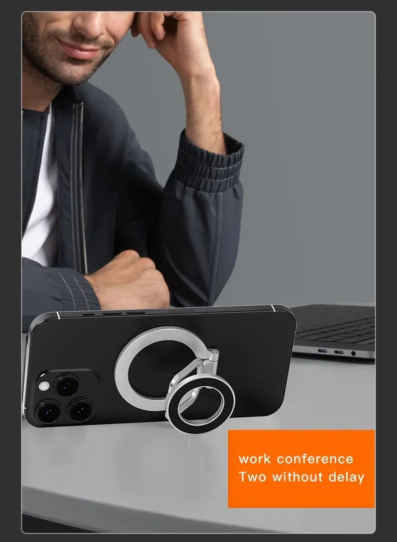 Silver magnetic phone ring holder attached to the back of a black smartphone, resting on a desk.