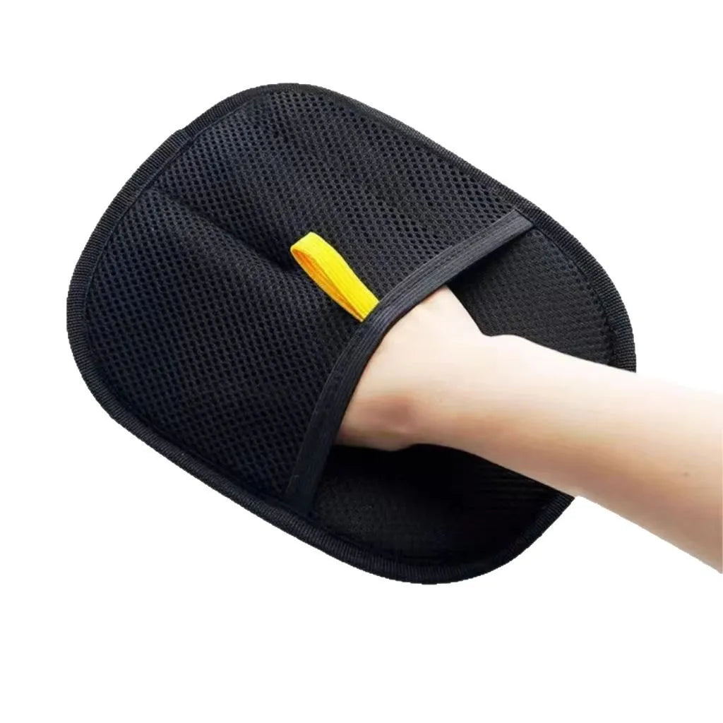 A black, textured mesh applicator mitt with a yellow finger loop, shown being worn on a hand against a white background.
