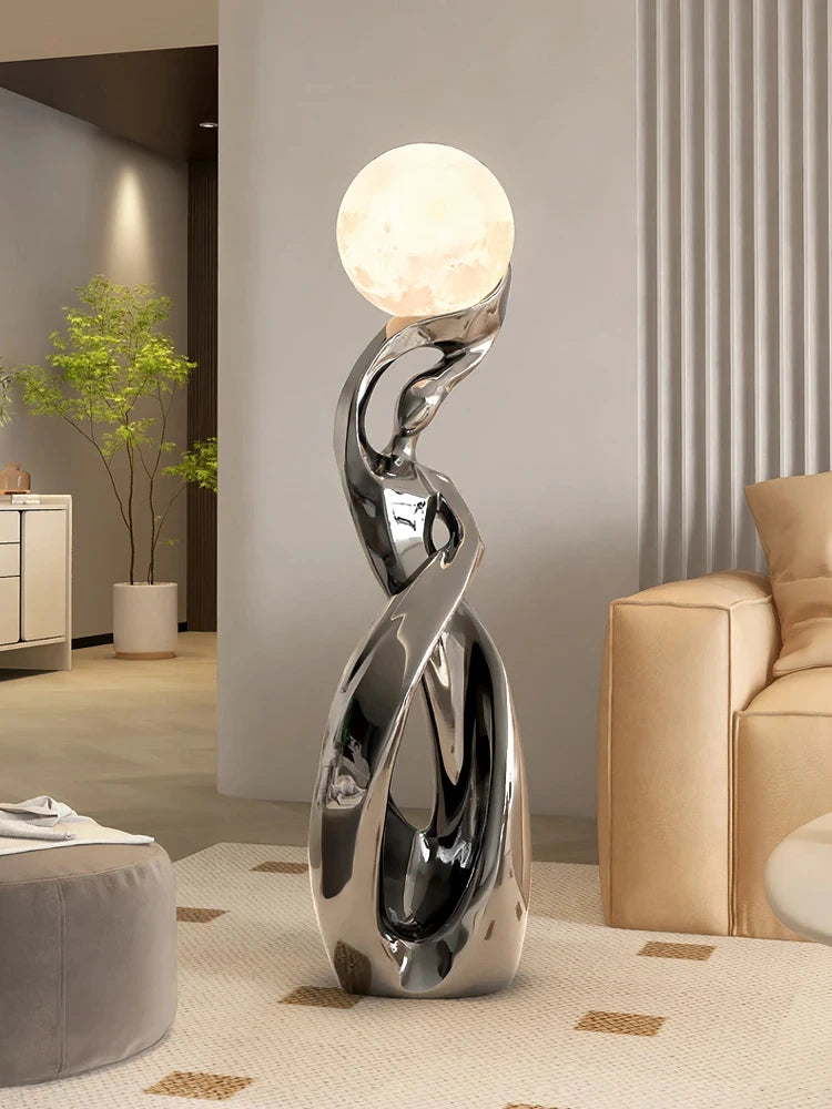 Modern chrome abstract floor ornament featuring a luminous, moon-like glowing sphere held by a fluid, sculpted base.