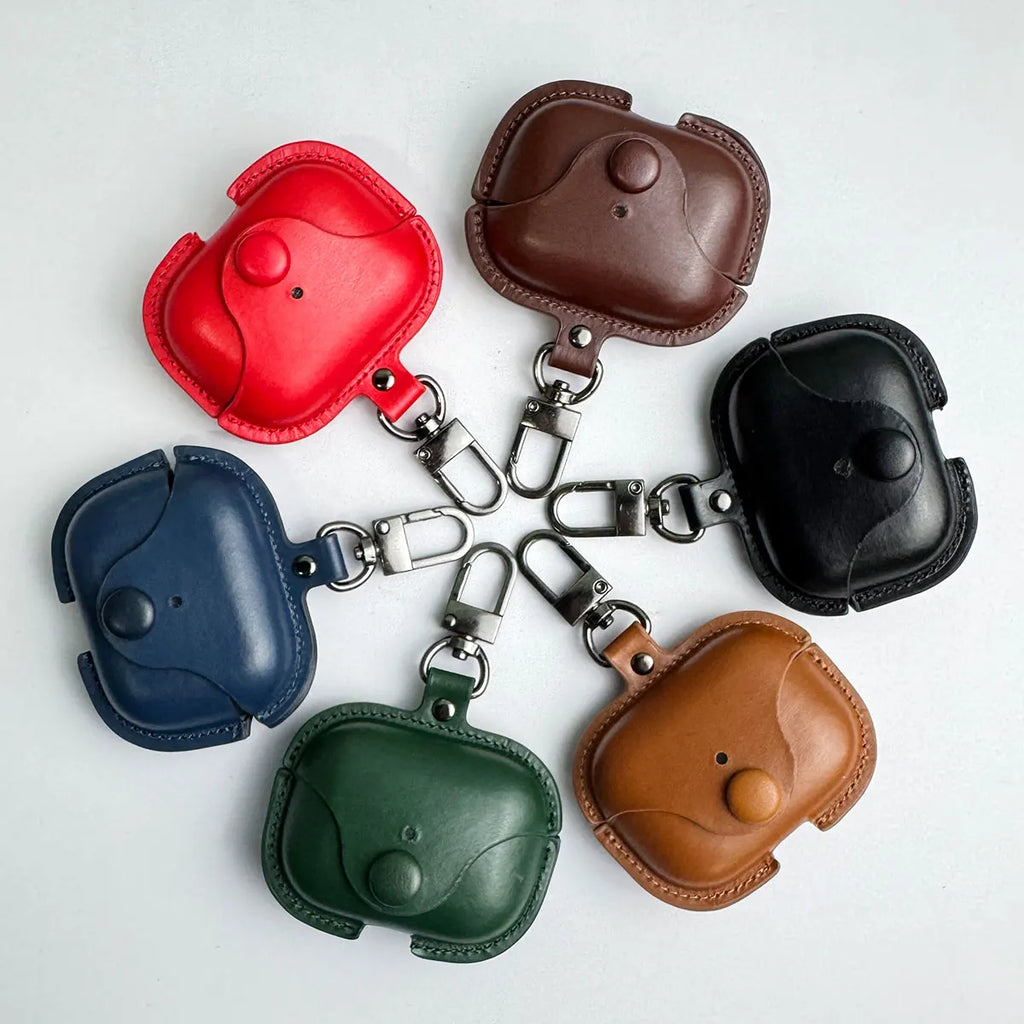 Assorted leather AirPods Pro cases with snap-button closure and metal clips in red, brown, black, tan, green, and blue.