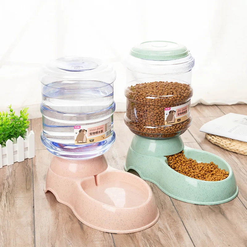 Two automatic pet feeders with speckle-finish pink and green bases, featuring clear 3.8L storage reservoirs.