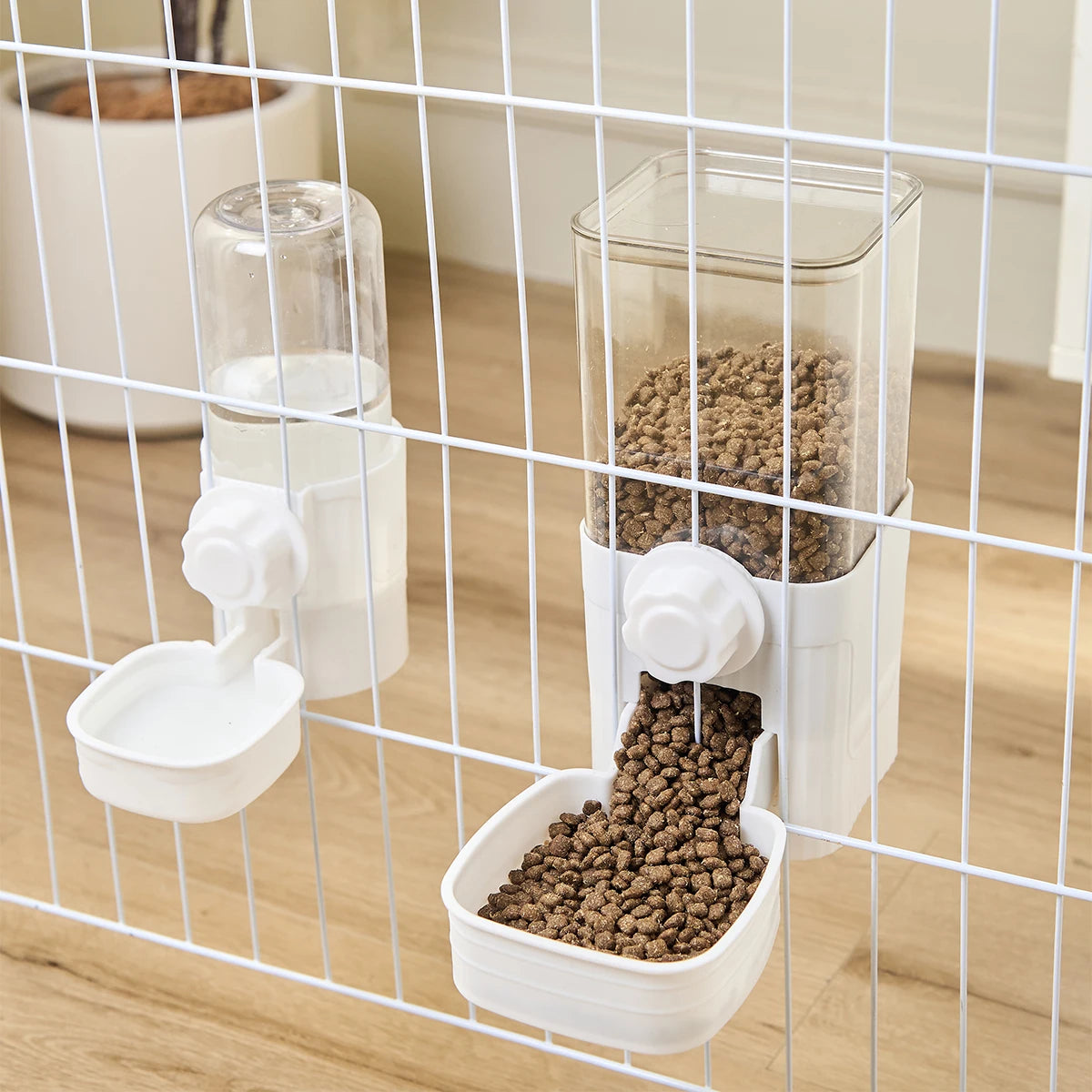 White hanging pet food and water dispensers with clear containers attached to a wire cage.