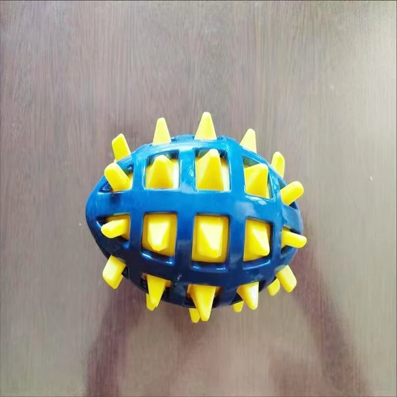 Blue and yellow rubber rugby ball dog toy with a spiky, cage-like design on a wooden surface.