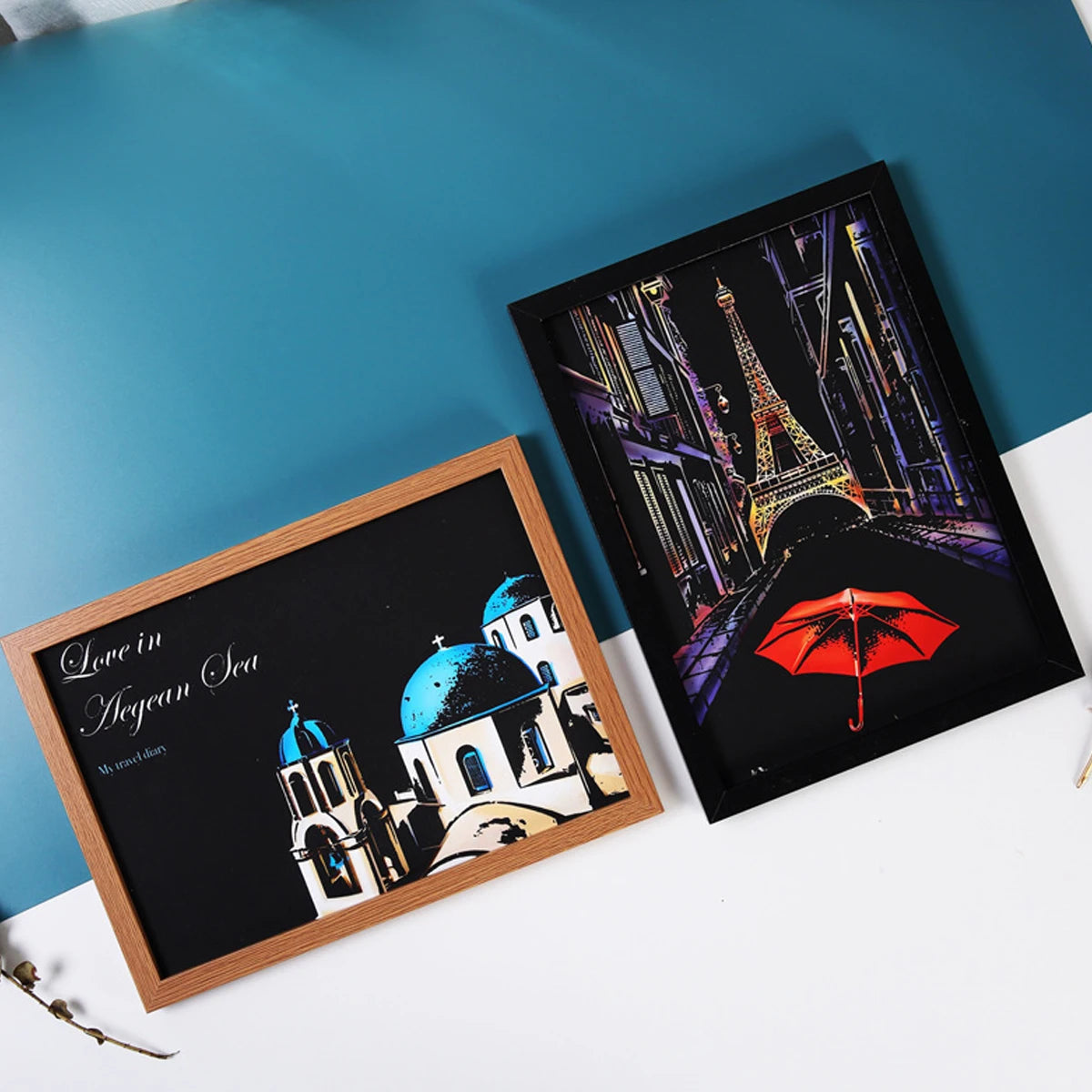 Two framed scratch-art prints featuring a Parisian Eiffel Tower scene and a Mediterranean Greek architecture design.