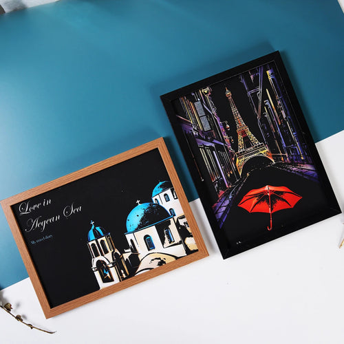Two framed scratch-art prints featuring a Parisian Eiffel Tower scene and a Mediterranean Greek architecture design.