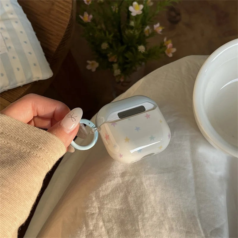 Clear AirPods 3 case with a pastel star print, featuring a light blue silicone ring, held by a hand.