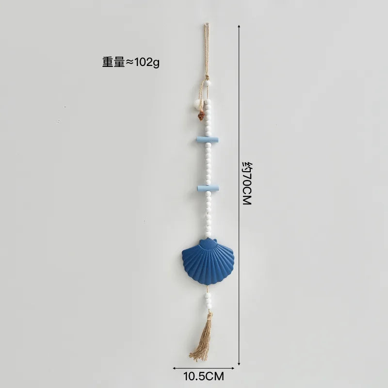 Boho wall hanging featuring white beads, blue wooden accents, a large blue seashell charm and a natural jute tassel.