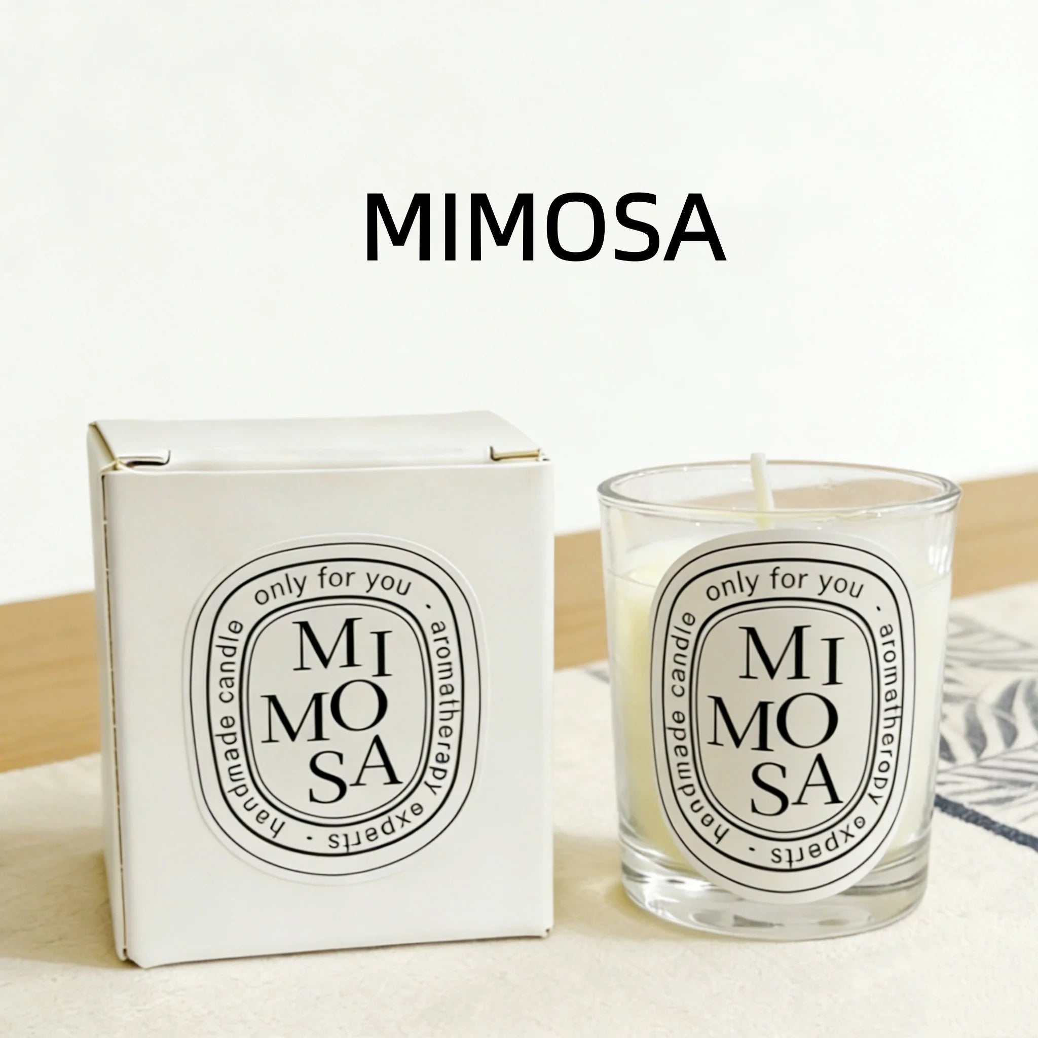 Mimosa scented aromatherapy candle in a glass jar with matching white box, both featuring a modern black oval label.