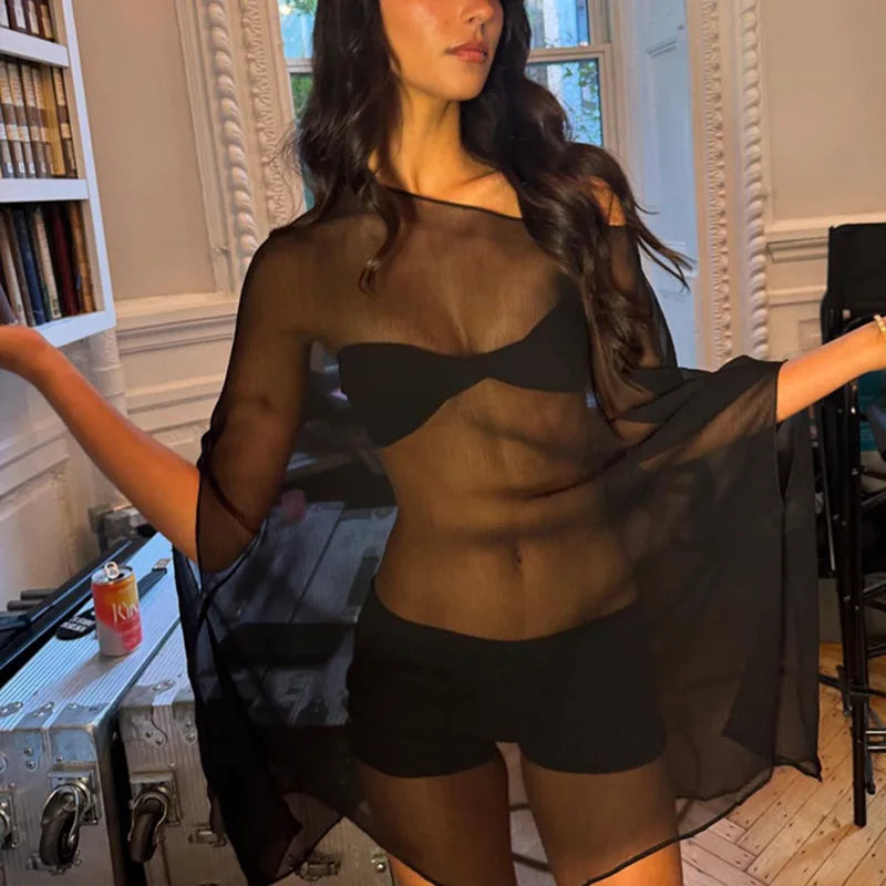 Woman wearing a black, sheer, off-the-shoulder long-sleeve cover-up over a matching black bikini set.