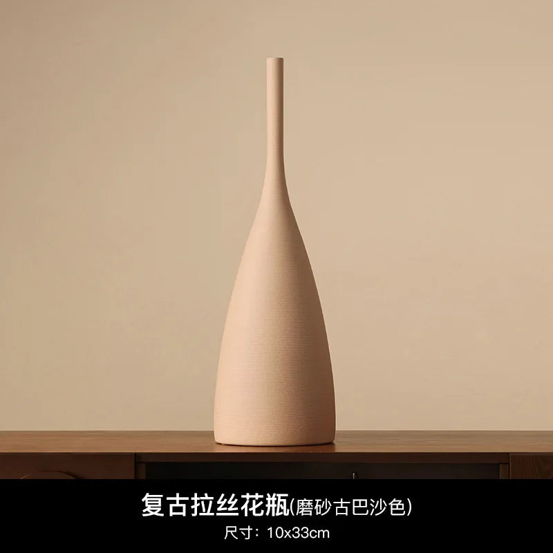 Tall, slender beige ceramic vase with a matte, textured finish and minimalist Wabi-Sabi design on a wooden surface.
