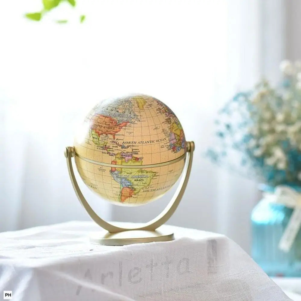 Vintage-style world globe with a soft cream finish and elegant gold-tone metal stand on a white cloth surface.