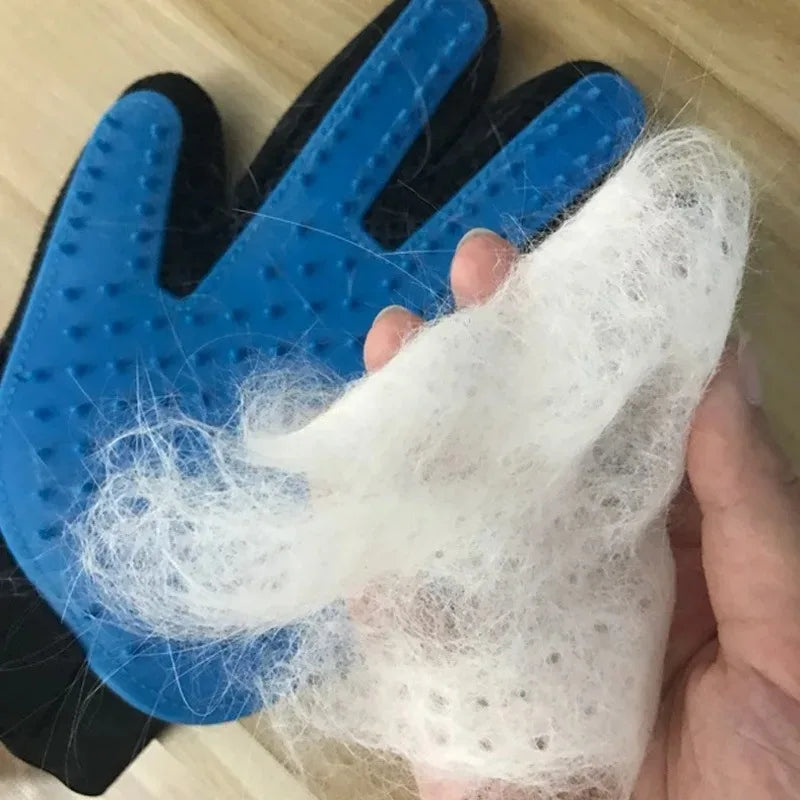 Blue and black silicone grooming glove covered in clumps of shed white pet hair being held by a hand.