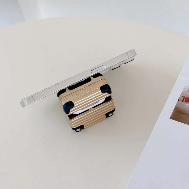 Gold suitcase-style protective case for AirPods, featuring a ridged hard-shell design with black corner accents.