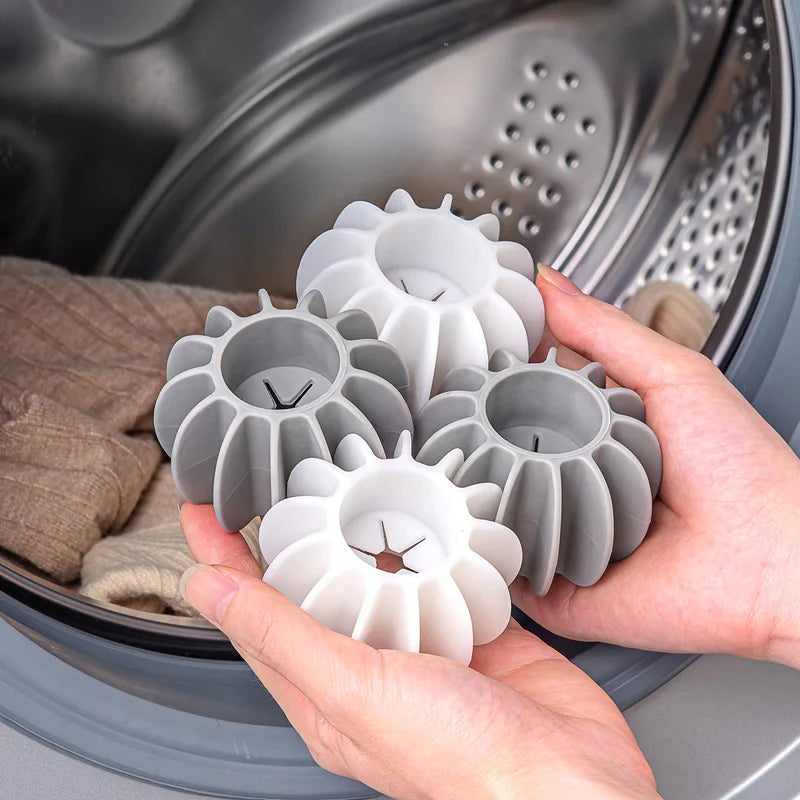 Hands holding four grey and white silicone laundry dryer balls in front of an open washing machine.