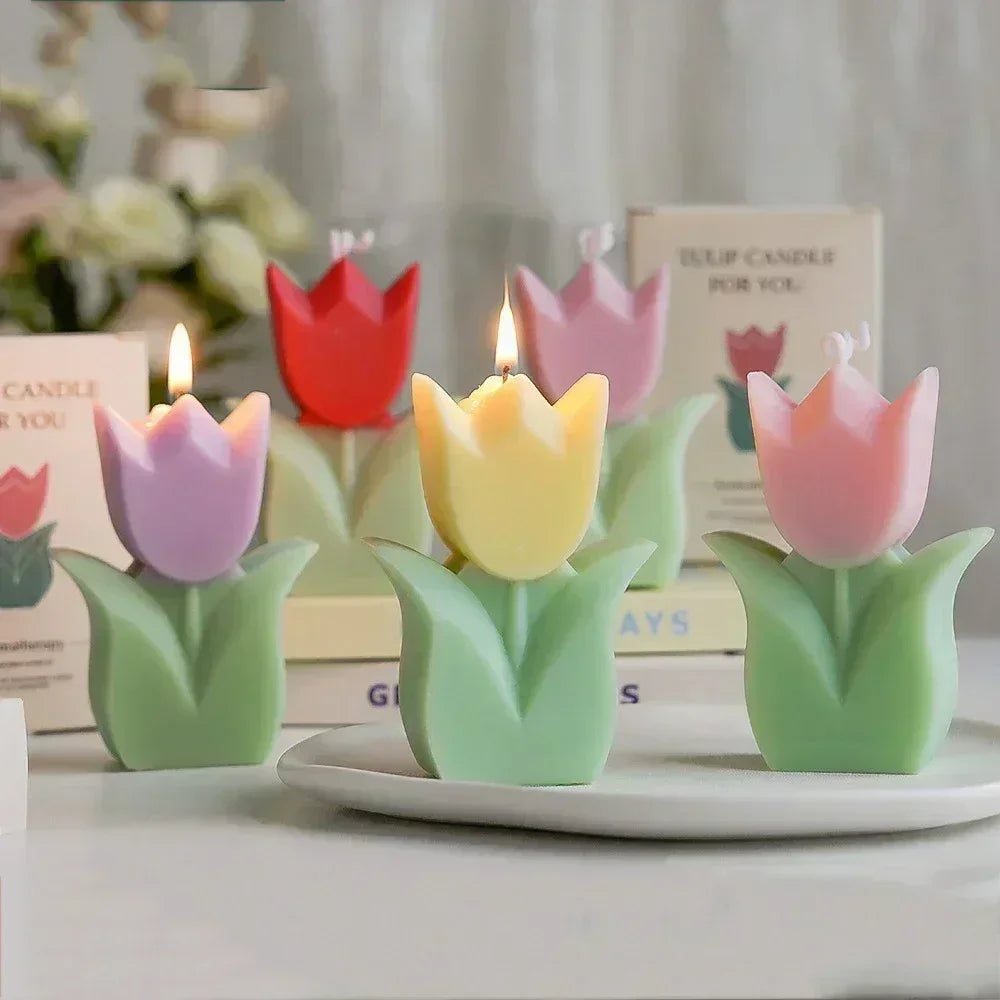 Assorted pastel-coloured tulip-shaped candles on green stems, some lit, arranged on a plate.