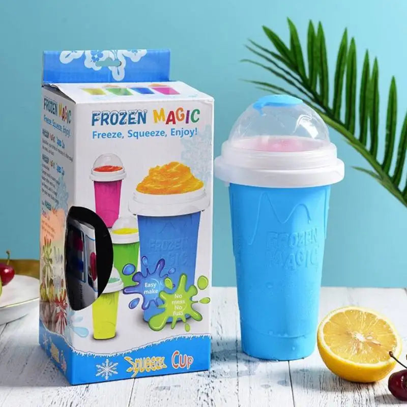 A blue slushy maker cup with a white lid next to its product box on a white wooden table with fruit nearby.