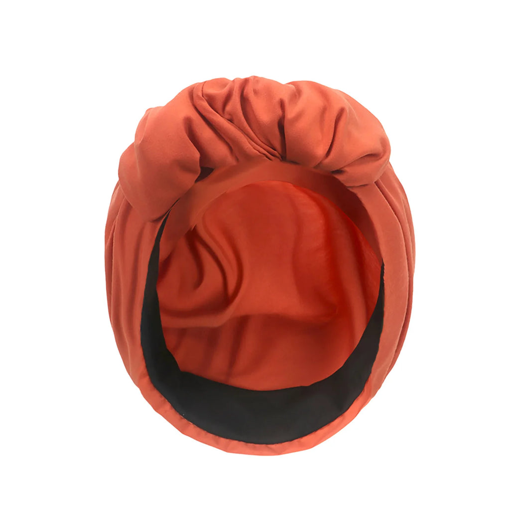 Rust-orange vintage style turban hat with a knotted front and black inner lining, seen from above.