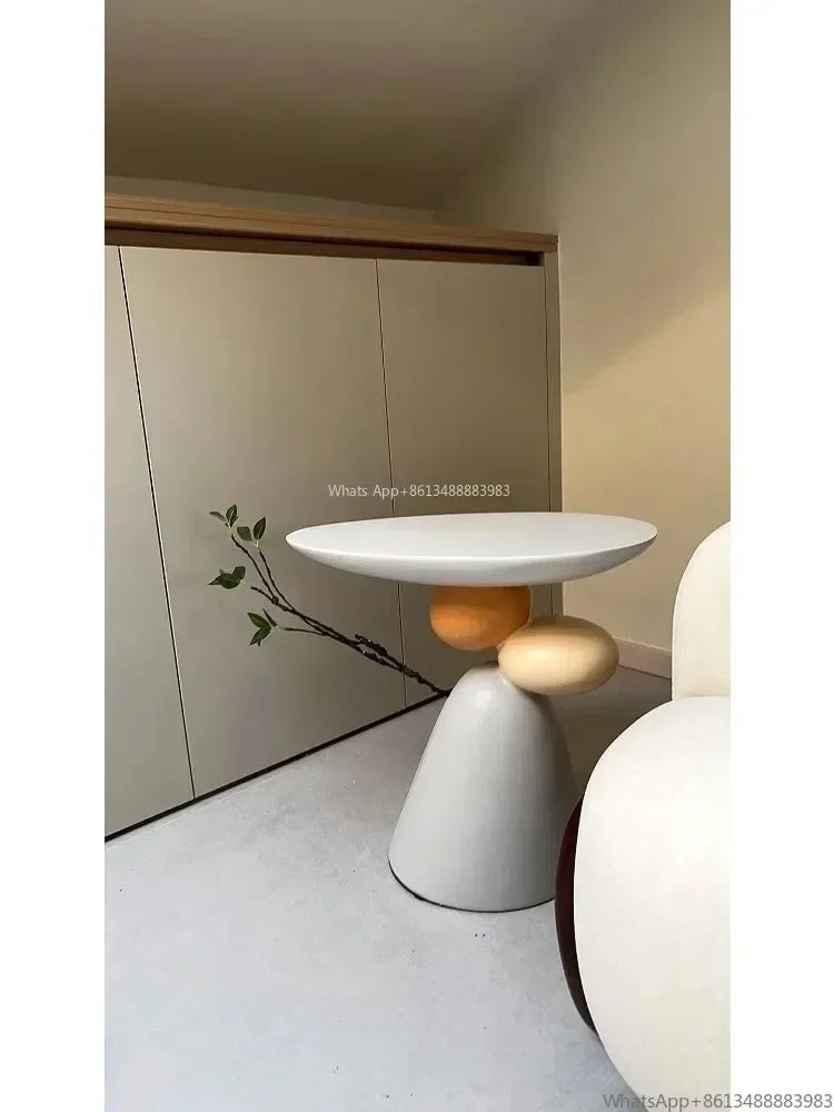 Minimalist cream side table with a sculptural base featuring rounded, contrasting accent shapes.