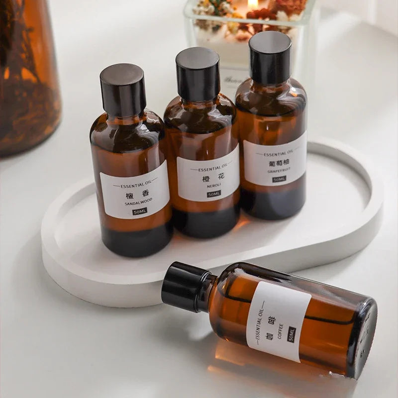 Four 50ml amber glass essential oil bottles with black caps and white labels, arranged on a white oval tray.