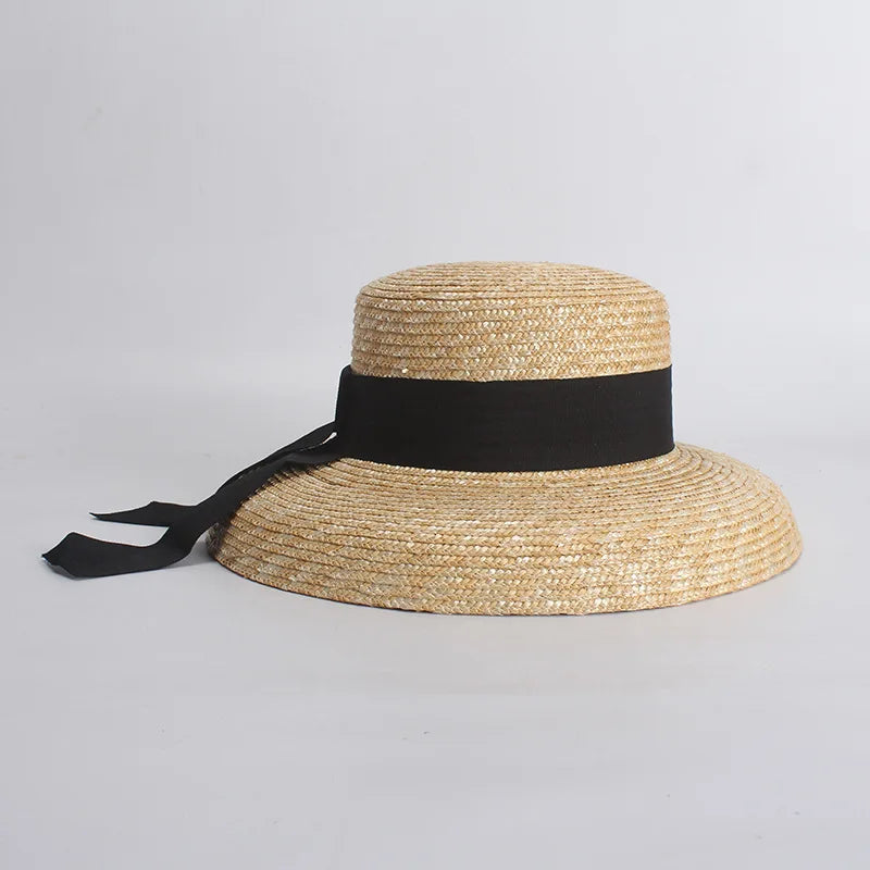 Elegant straw sun hat with a wide brim and a black ribbon tie, set against a plain light background.