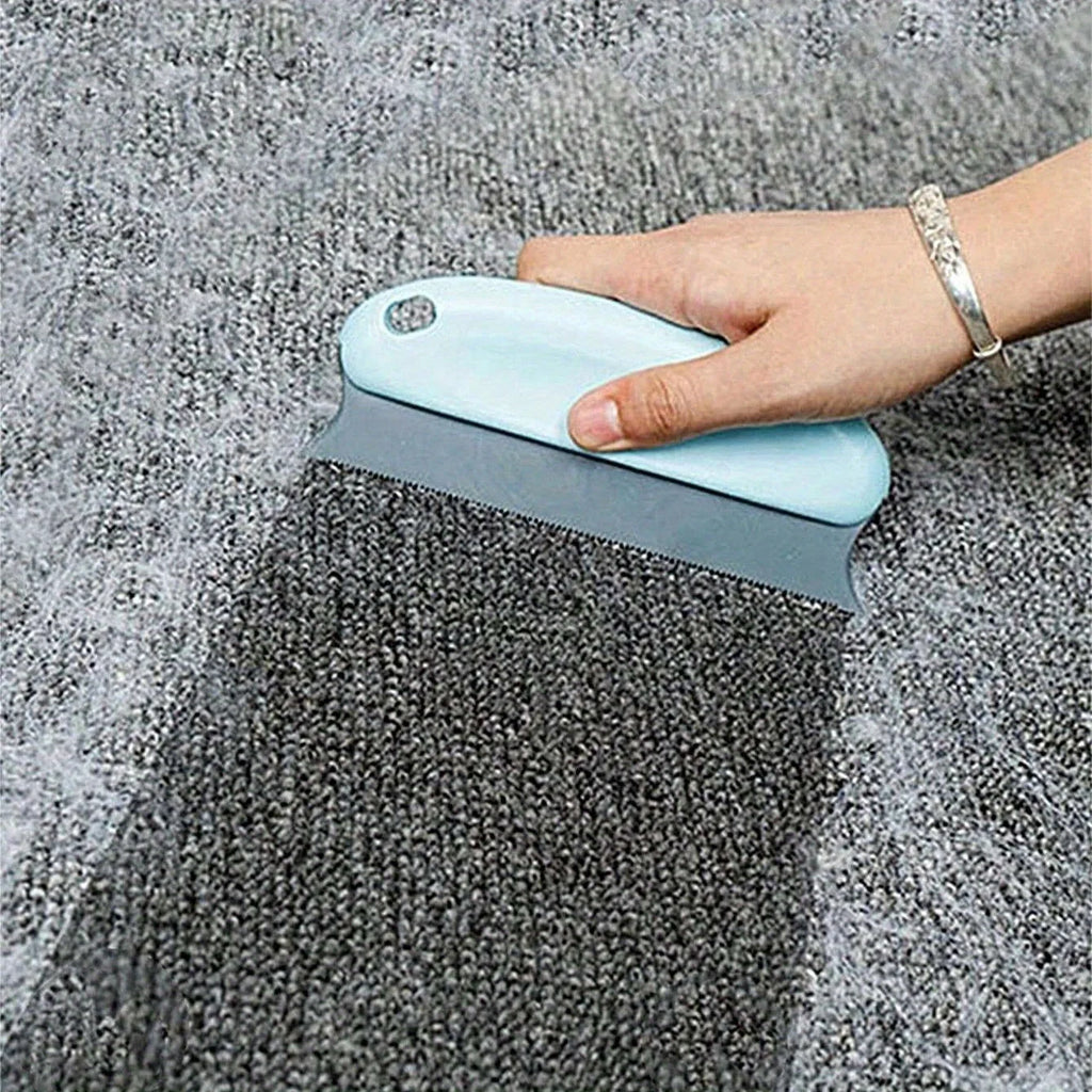 Hand using a pale blue handheld lint remover tool to clear fuzz from a grey carpet.