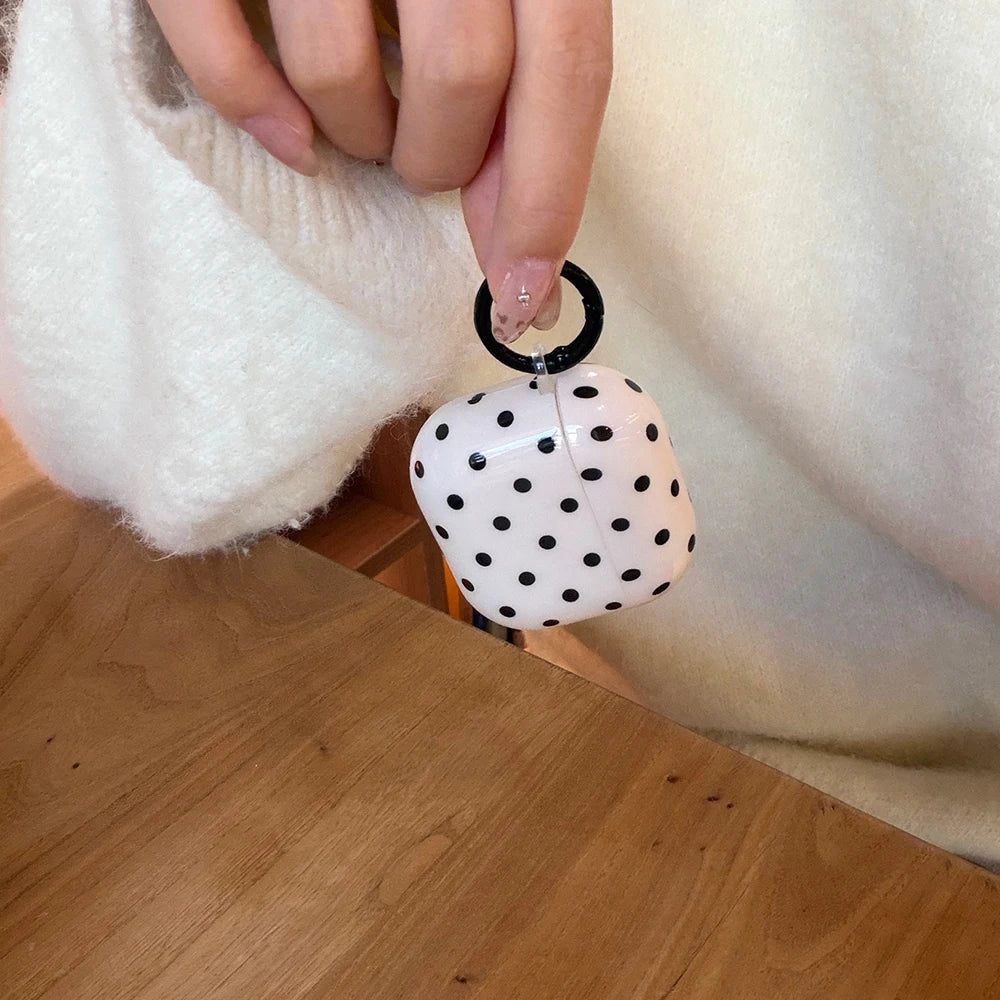White, black-spotted hard shell AirPods case with a black ring attachment, held by hand.