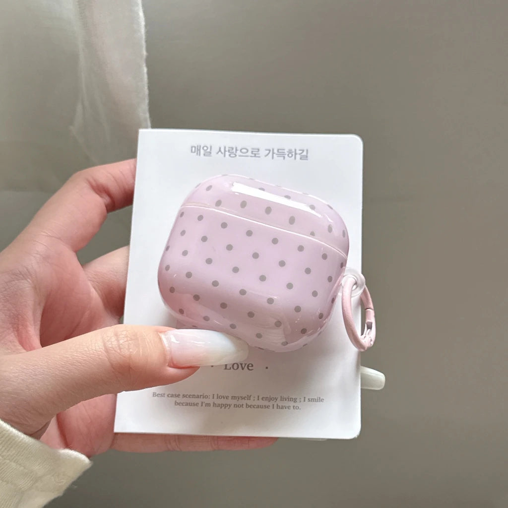 Glossy pink AirPods case with grey polka dots and a side attachment loop on display packaging.